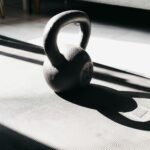 Kettlebell in bright sunlight casting shadow on gym mat indoors, perfect for fitness themes.