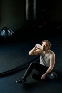 Adult man resting in a gym after a workout, drinking water from a bottle.