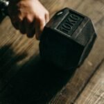 A close-up shot of a hand gripping a 10kg dumbbell on a wooden floor, perfect for fitness themes.